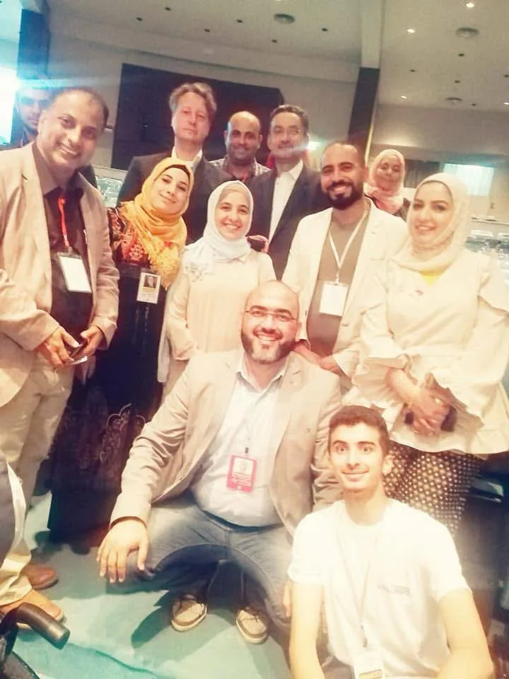 A group of conference attendees wearing lanyards gathered close for a photo, Dr. Abu-Sheikha crouching at the centre